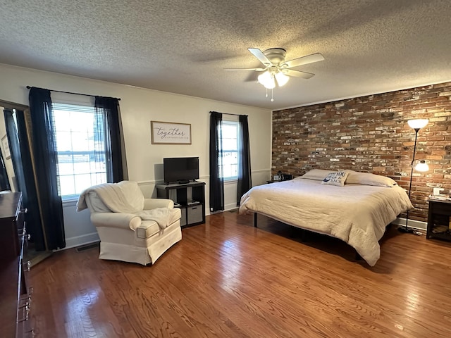 bedroom with ceiling fan, a textured ceiling, brick wall, and wood finished floors