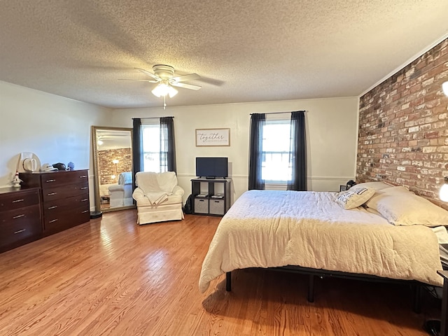 bedroom featuring ceiling fan, multiple windows, a textured ceiling, and light wood-style flooring