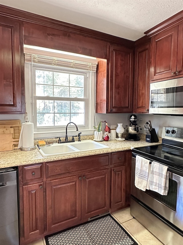 kitchen featuring light countertops, appliances with stainless steel finishes, light tile patterned flooring, a sink, and a textured ceiling