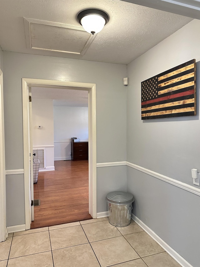 hall with light tile patterned floors, attic access, visible vents, baseboards, and a textured ceiling