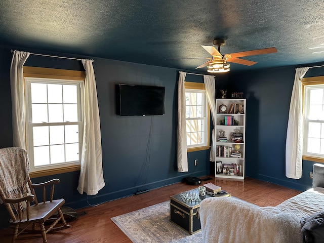 living area with ceiling fan, a textured ceiling, baseboards, and dark wood-type flooring