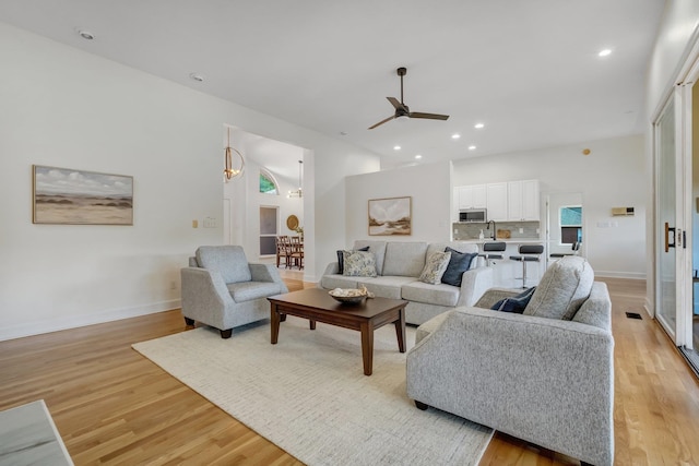 living room featuring light wood-type flooring, ceiling fan with notable chandelier, and sink