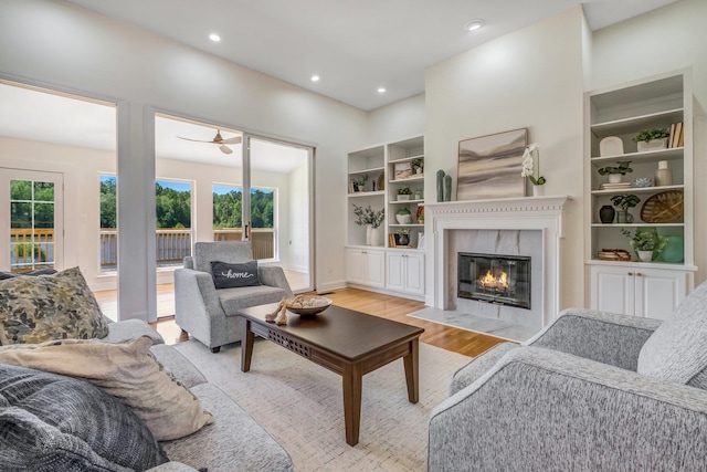 living room with light wood-type flooring, built in features, and ceiling fan