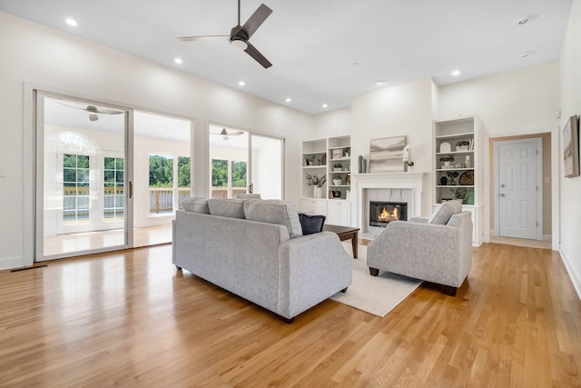 living room featuring built in shelves, light hardwood / wood-style floors, and ceiling fan