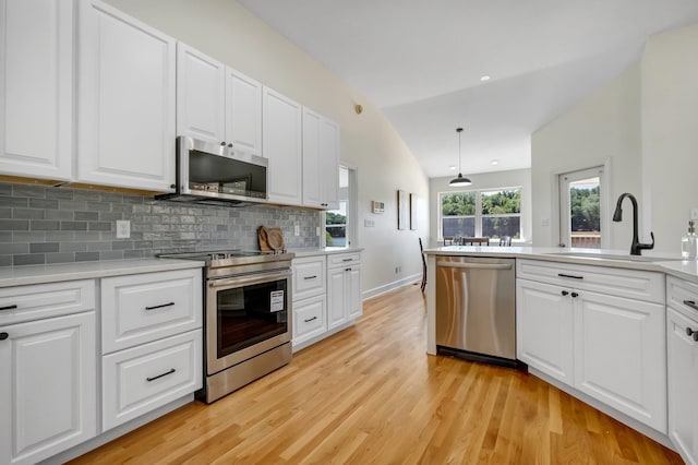 kitchen featuring appliances with stainless steel finishes, decorative light fixtures, sink, vaulted ceiling, and white cabinets