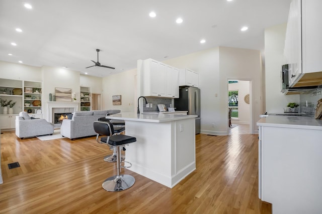 kitchen with appliances with stainless steel finishes, tasteful backsplash, a breakfast bar area, light hardwood / wood-style flooring, and white cabinets