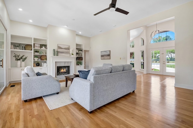 living room with built in shelves, french doors, light hardwood / wood-style floors, a high ceiling, and ceiling fan with notable chandelier