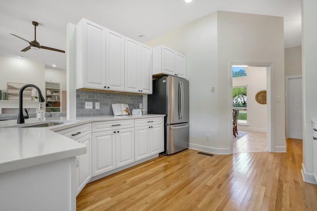 kitchen featuring light hardwood / wood-style floors, stainless steel refrigerator, white cabinetry, sink, and tasteful backsplash