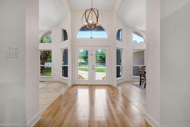 foyer entrance with french doors, a towering ceiling, a chandelier, and light wood-type flooring