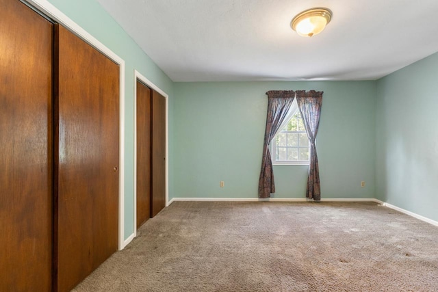 unfurnished bedroom featuring multiple closets, baseboards, and carpet