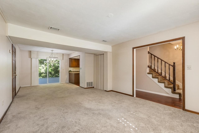 unfurnished living room with an inviting chandelier, carpet, stairs, baseboards, and visible vents
