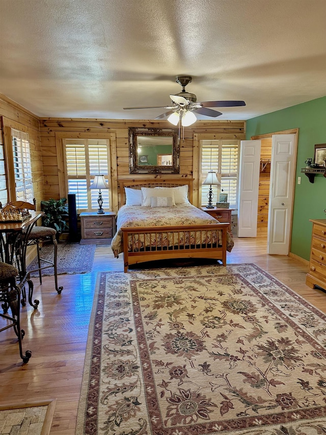 bedroom featuring light wood-style floors, wooden walls, ceiling fan, and a textured ceiling