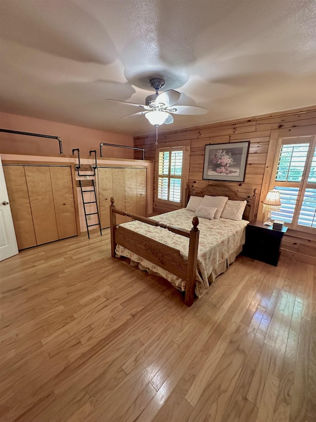bedroom with multiple windows, ceiling fan, wood walls, and light wood-style floors