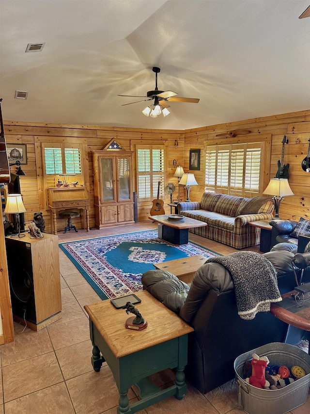living room with a wealth of natural light, wooden walls, ceiling fan, and visible vents
