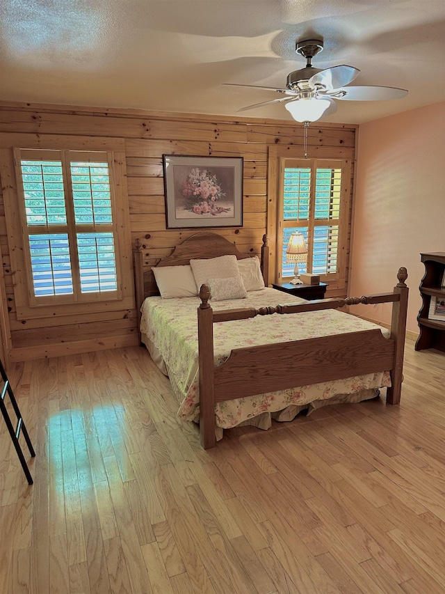 bedroom with light wood-type flooring, ceiling fan, and wood walls
