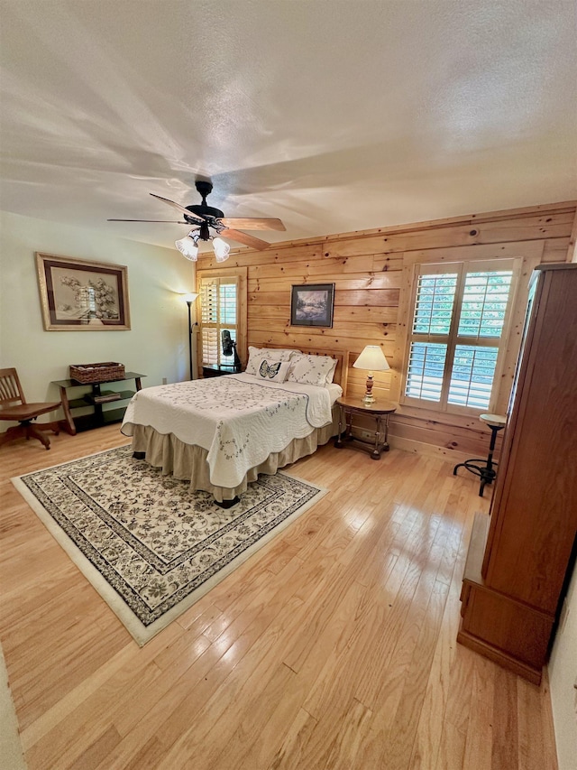 bedroom with wood walls, a ceiling fan, a textured ceiling, and light wood finished floors