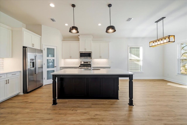 kitchen with stainless steel appliances, an island with sink, white cabinets, and hanging light fixtures