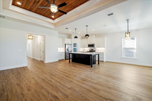 kitchen with a center island with sink, decorative light fixtures, appliances with stainless steel finishes, and a raised ceiling