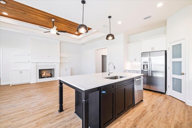 kitchen featuring appliances with stainless steel finishes, an island with sink, white cabinets, a tray ceiling, and sink