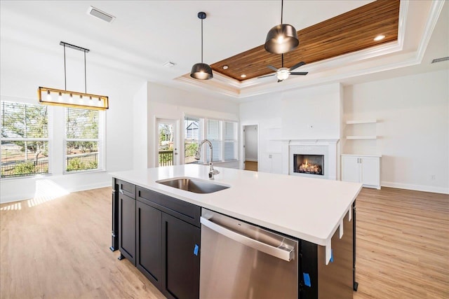 kitchen with an island with sink, sink, stainless steel dishwasher, a raised ceiling, and pendant lighting