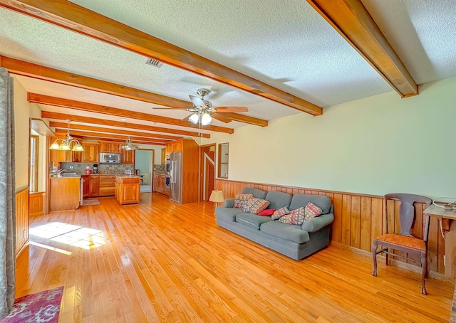 unfurnished living room with sink, beamed ceiling, a textured ceiling, ceiling fan with notable chandelier, and light wood-type flooring