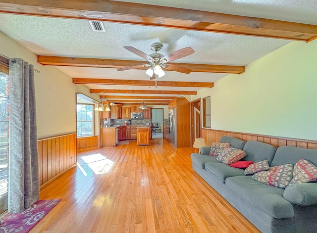 unfurnished living room featuring beam ceiling, ceiling fan, light hardwood / wood-style flooring, and a textured ceiling