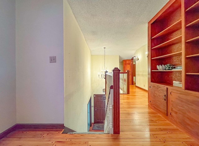 corridor featuring a chandelier, a textured ceiling, and light wood-type flooring