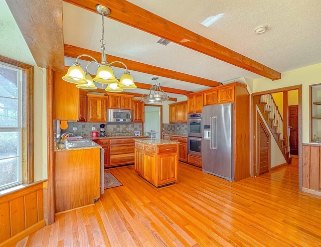 kitchen with appliances with stainless steel finishes, a chandelier, decorative light fixtures, a kitchen island, and light wood-type flooring