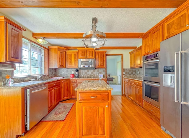 kitchen with beam ceiling, tasteful backsplash, light hardwood / wood-style floors, a center island with sink, and appliances with stainless steel finishes