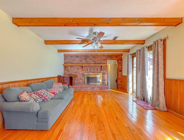 living room featuring a fireplace, a textured ceiling, light hardwood / wood-style flooring, and ceiling fan