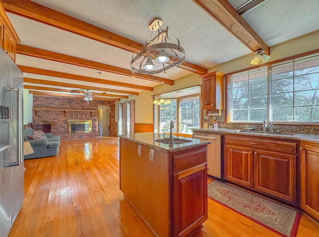 kitchen featuring stainless steel appliances, sink, pendant lighting, a fireplace, and an island with sink