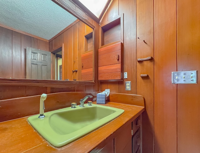 bathroom featuring vanity, a textured ceiling, crown molding, and wooden walls