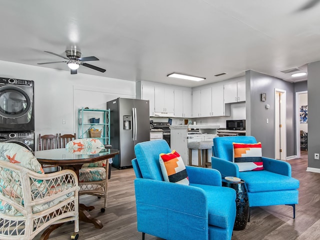 kitchen featuring appliances with stainless steel finishes, stacked washing maching and dryer, ceiling fan, light hardwood / wood-style flooring, and white cabinetry