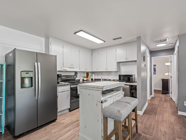 kitchen with a breakfast bar, white cabinets, a kitchen island, appliances with stainless steel finishes, and light hardwood / wood-style floors