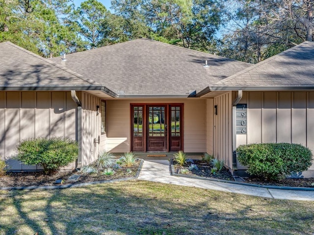 property entrance featuring board and batten siding, a lawn, and a shingled roof