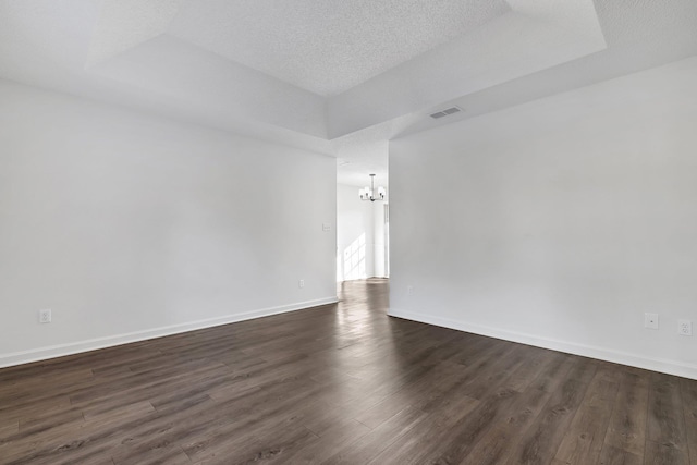 spare room with a textured ceiling, a tray ceiling, a notable chandelier, and dark wood-type flooring