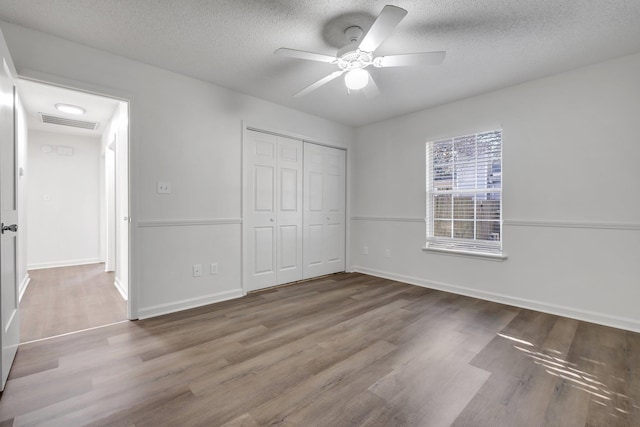 unfurnished bedroom featuring ceiling fan, a closet, a textured ceiling, and hardwood / wood-style flooring