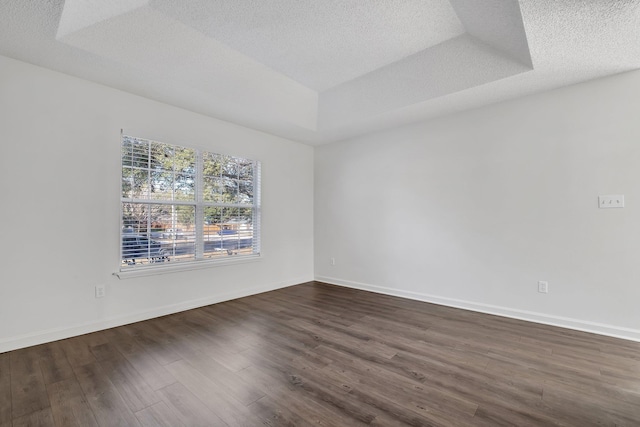 unfurnished room with a textured ceiling, dark hardwood / wood-style floors, and a tray ceiling