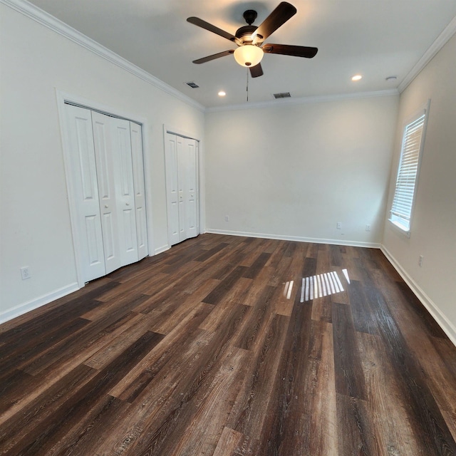 unfurnished bedroom with ceiling fan, dark hardwood / wood-style floors, ornamental molding, and multiple closets