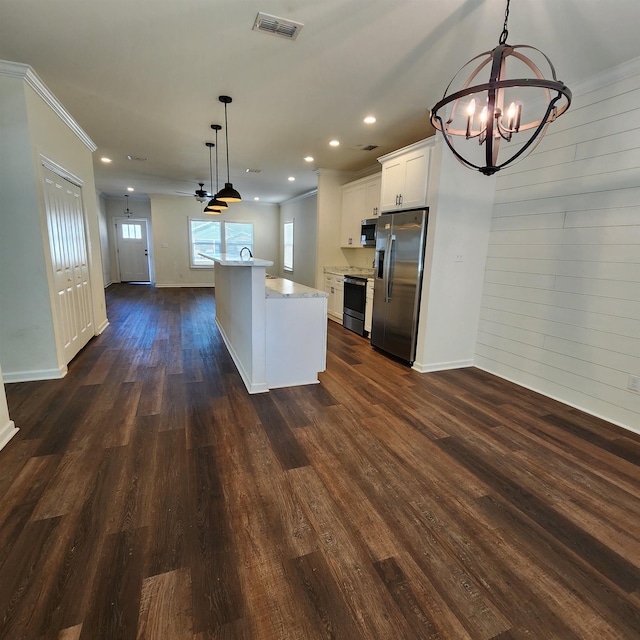 kitchen featuring stainless steel appliances, pendant lighting, white cabinets, a kitchen island, and wood walls