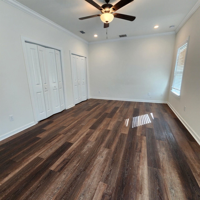 unfurnished bedroom featuring ceiling fan, dark hardwood / wood-style flooring, crown molding, and multiple closets