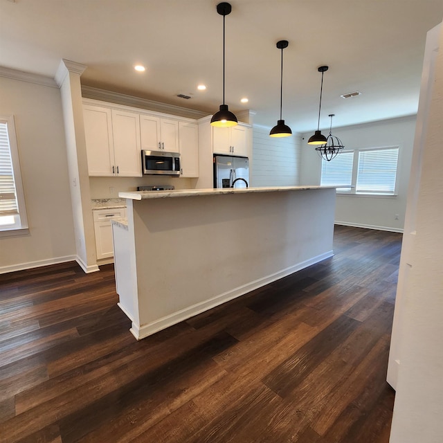 kitchen with dark hardwood / wood-style flooring, pendant lighting, a kitchen island with sink, white cabinets, and appliances with stainless steel finishes