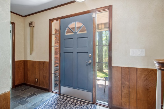entryway with a wainscoted wall, a wealth of natural light, crown molding, wooden walls, and stone finish floor