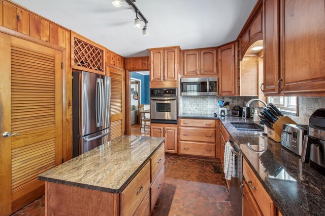 kitchen with backsplash, appliances with stainless steel finishes, dark stone countertops, a sink, and brown cabinetry