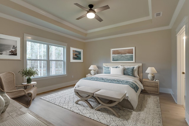 bedroom with ceiling fan, a tray ceiling, crown molding, and light wood-type flooring