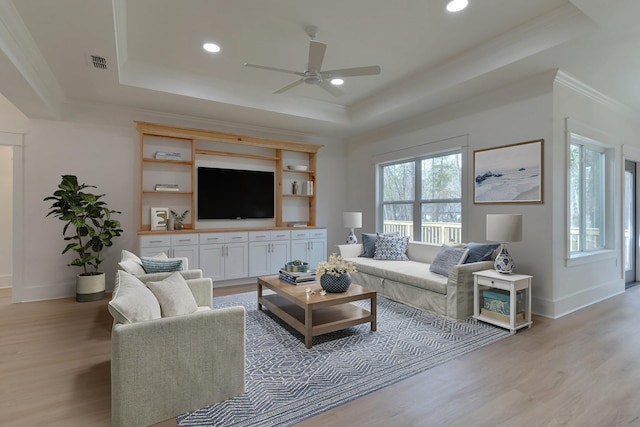 living room with a raised ceiling, ornamental molding, and light hardwood / wood-style floors