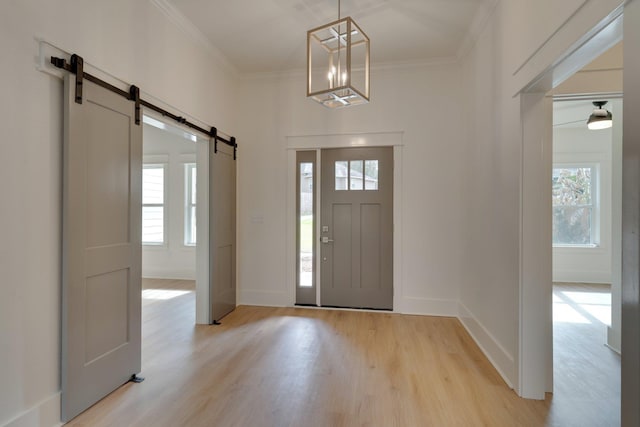 foyer with ornamental molding, a barn door, light hardwood / wood-style flooring, and an inviting chandelier