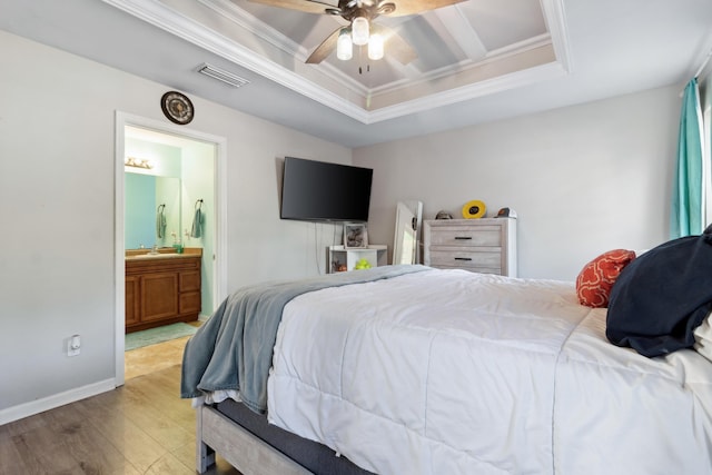 bedroom featuring ceiling fan, a raised ceiling, light hardwood / wood-style flooring, ensuite bathroom, and ornamental molding