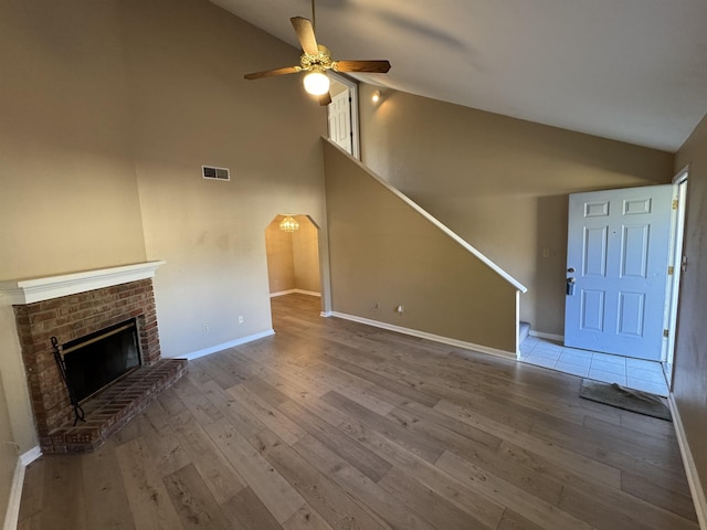 unfurnished living room with light wood-type flooring, high vaulted ceiling, a brick fireplace, and ceiling fan