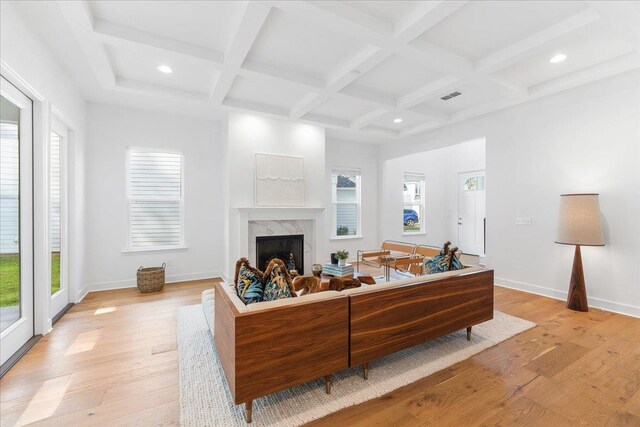 living room featuring light wood-type flooring, a fireplace, beamed ceiling, and a healthy amount of sunlight